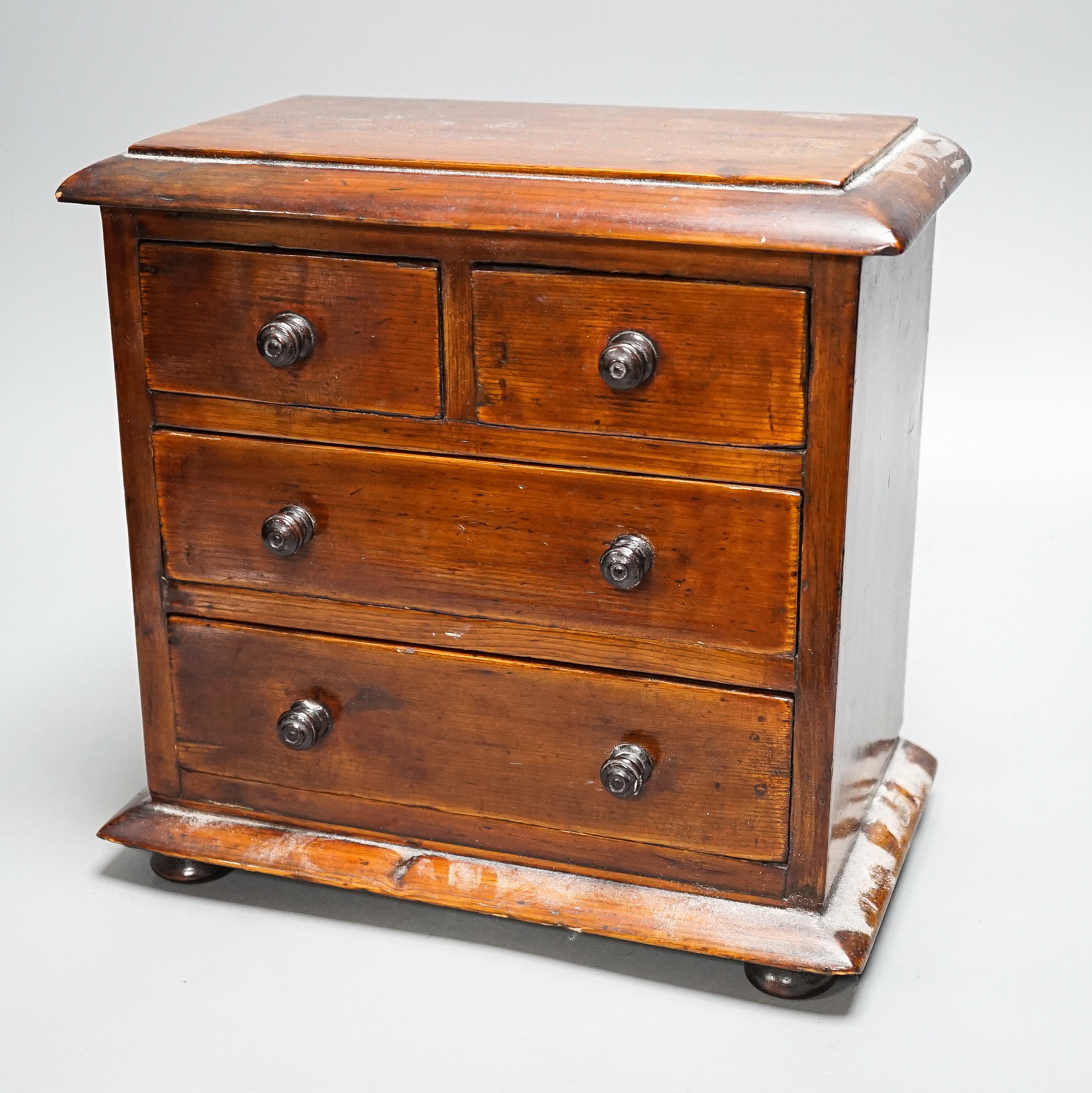 A Victorian stained pine miniature chest of drawers, 27 cms high.